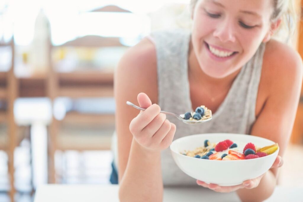 Smiling woman eating a bowl of healthy cereal and fruit